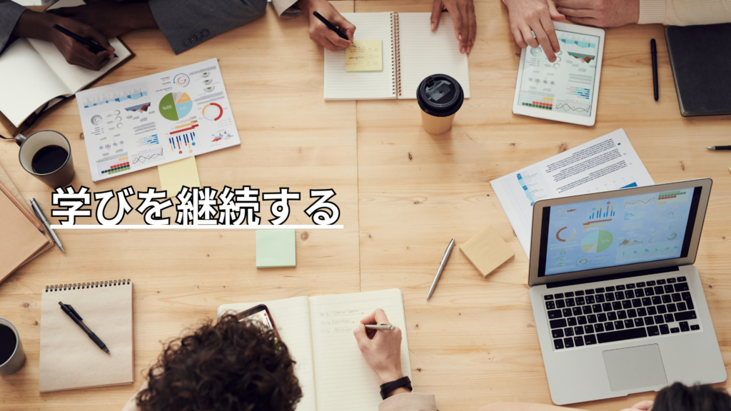 木のテーブルの上で資料やパソコンを広げ、ノートをとる5人の手元