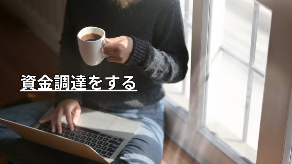 窓際でコーヒー片手にパソコンを操作するあぐら姿勢の女性の首から下